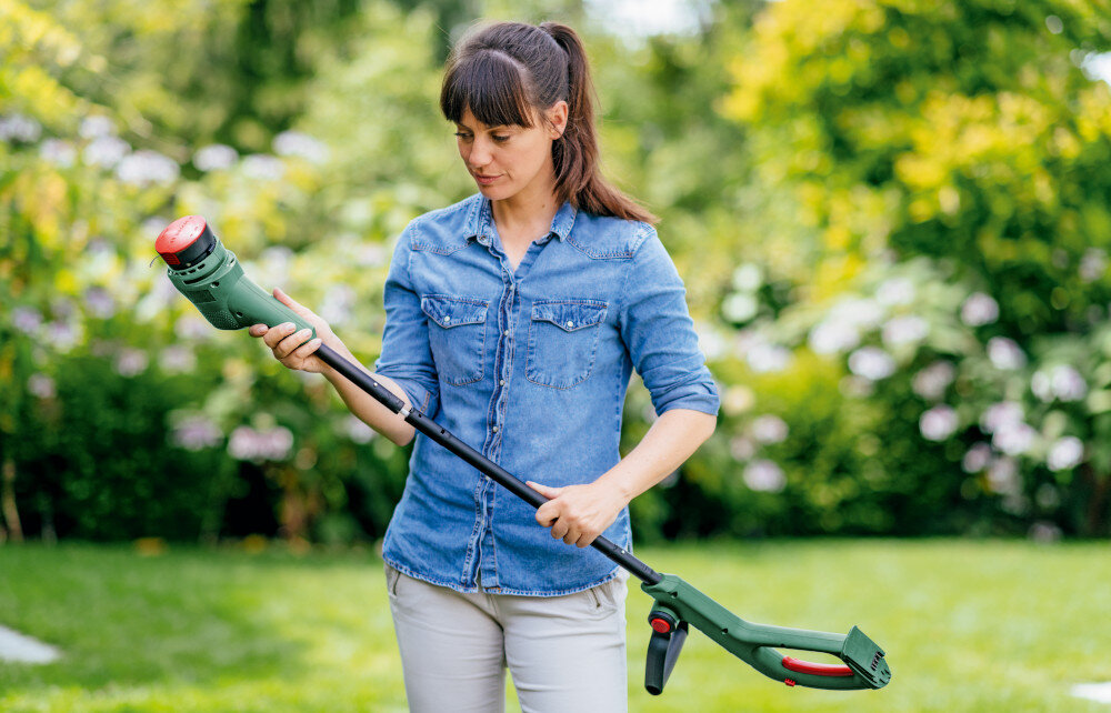 Podkaszarka akumulatorowa BOSCH EasyGrassCut 06008C1A04 ogród osoba trzyma podkaszarkę w dłoniach składa ją przycięcie sześciu kortów tenisowych przy użyciu jednego akumulatora o pojemności 2,0 Ah czas ładowania akumulatora w około dwie godziny