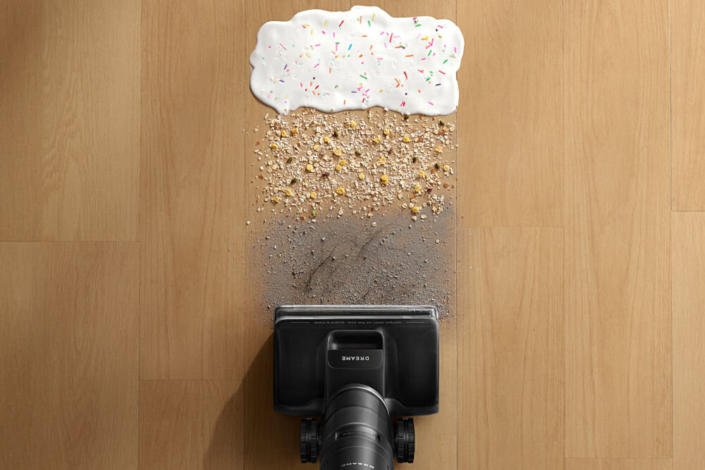 Odkurzacz z napisem \'DREAME\' usuwa różne rodzaje zabrudzeń z drewnianej podłogi, w tym płyn, okruchy i kurz.
