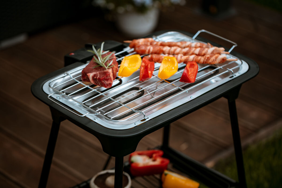 Grill elektryczny ADLER AD 6602, moc, operowanie, grillowanie, wysoka, w tle taras na pierwszym planie grill na nóżkach z potrawami na ruszcie