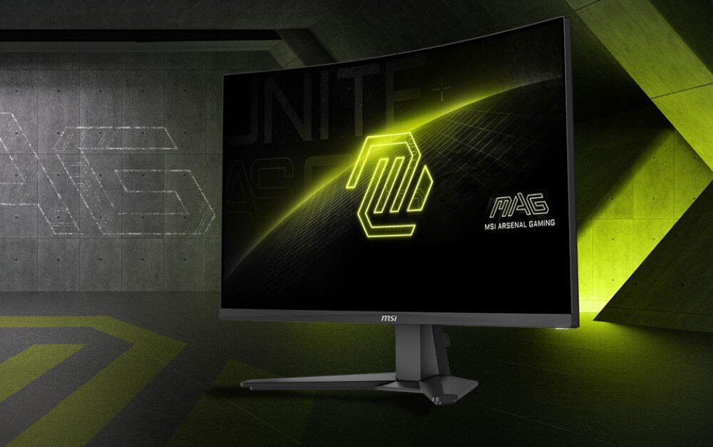 Monitor MSI Mag 276CF E20 Zakrzywiony monitor gamingowy ustawiony pod kątem na tle surowego, betonowego wnętrza z zielonymi akcentami świetlnymi