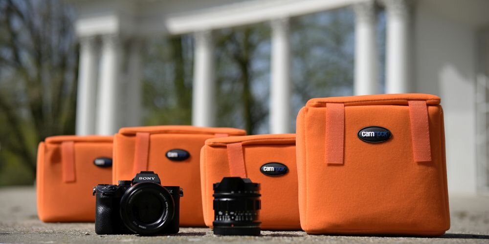 Na zdjęciu widoczne są cztery pomarańczowe wkłady fotograficzne z logo \'camrock\' oraz aparat fotograficzny i obiektyw na tle kolumnady.