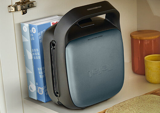 Opiekacz SW862B przechowywany pionowo w kuchennej szafce obok książek kucharskich i naczyń.