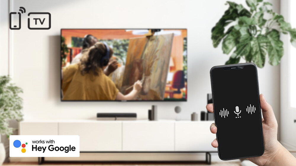 Telewizor TELEFUNKEN TFL-65AEU2000 - Wydawaj komendy głosowe, Asystent Google, ręka trzymająca telefon, telewizor zawieszony na ścianie w salonie