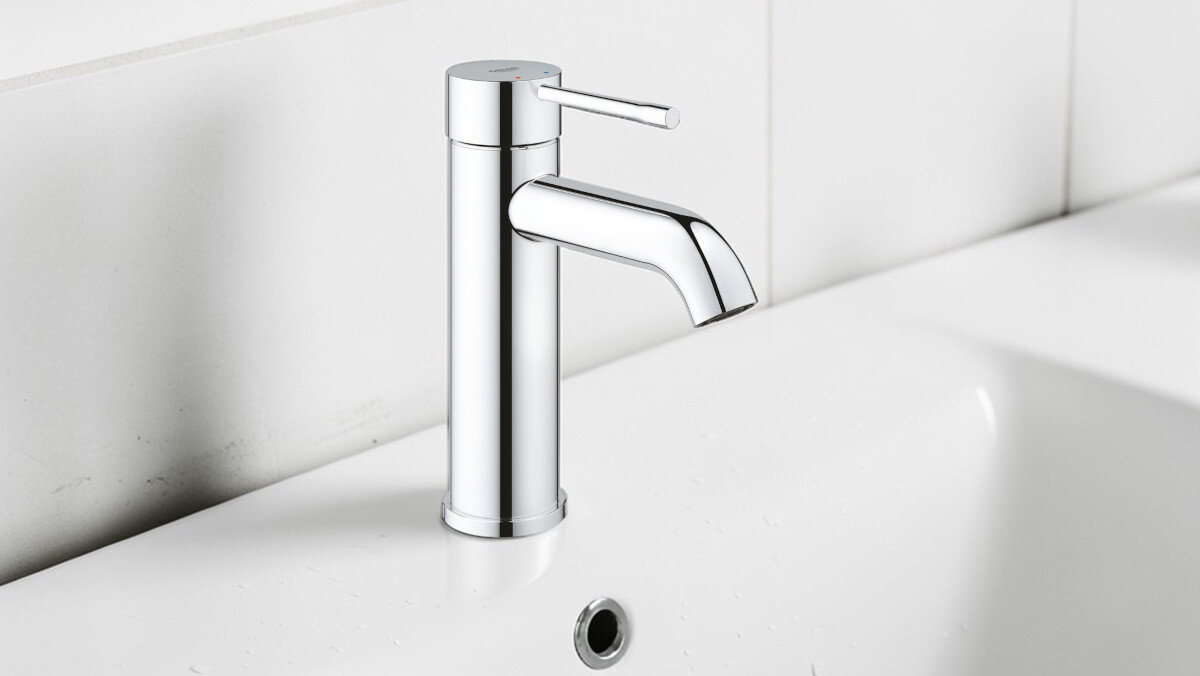 BATERIA UMYWALKOWA GROHE ESSENCE STOJĄCA 23590001 CHROM Zdjęcie pokazuje chromowaną baterię stojącą zamontowaną na białej umywalce o gładkiej, minimalistycznej formie. Tło stanowią jasne płytki, podkreślające wygląd armatury design wygląd styl chrom