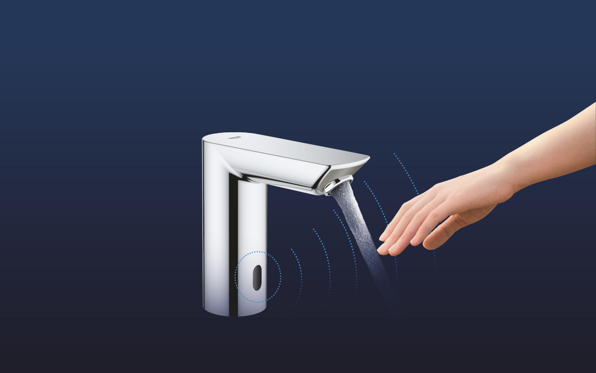 BATERIA UMYWALKOWA GROHE BAU COSMOPOLITAN E ELEKTRONICZNA 36451000 CHROM Ilustracja pokazuje chromowaną baterię bezdotykową, z której wypływa woda w momencie zbliżenia dłoni, a wokół widoczne są graficzne fale sygnalizujące działanie czujnika. Całość umieszczona jest na ciemnym, jednolitym tle podkreślającym produkt czujnik podczerwieni bezdotykowa łazienkowa automatyczne uruchamianie wody programowanie czujnika pilot zdalnego sterowania