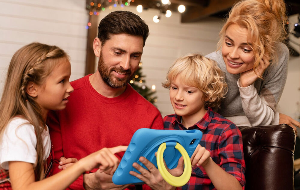 Tablet OSCAL Pad 60 Kids 10.1 cali 4/128 GB Wi-Fi Niebieski prezentacja urządzenia mężczyzna trzymający tablet wśród dzieci i kobiety w pokoju dziennym