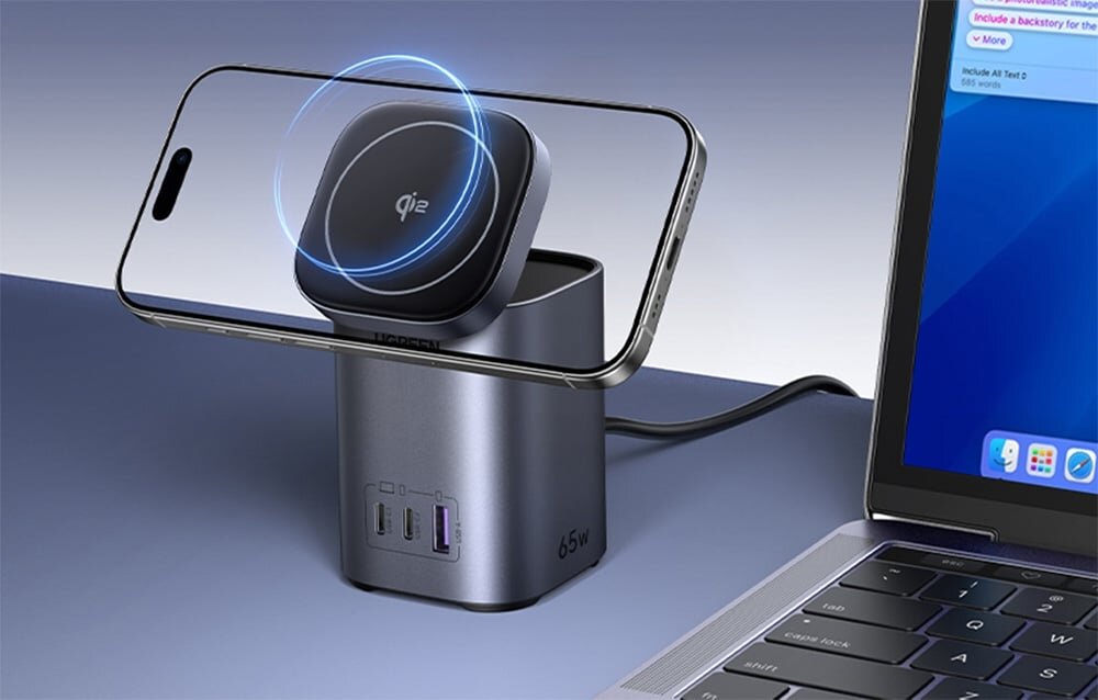 Na obrazie widoczna jest ładowarka z trzema portami (2x USB-C, 1x USB) oraz telefon umieszczony na bezprzewodowej podstawce z oznaczeniem \'qi\'. Obok znajduje się laptop, a na ładowarce widnieje napis \'65W\'.