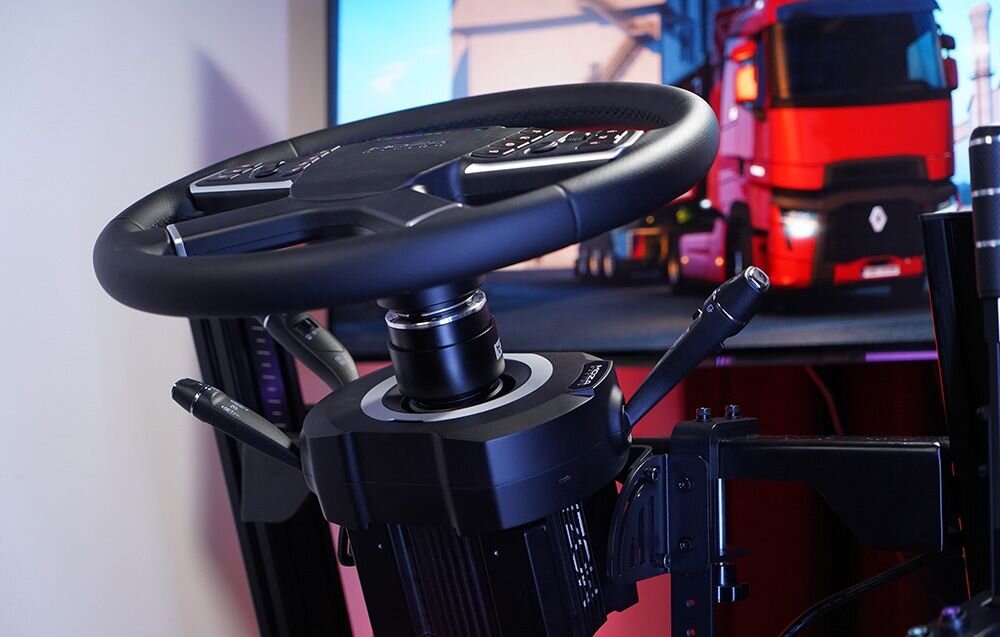 Manetki MOZA Racing RS065 Kierownica gaimngowa stojąca naprzeciwko monitora z wyświetlanym samochodem ciężarowym kompatybilność bazy MOZA przedłużki wsporniki dopasowanie ustawień adaptery bazy innych producentów