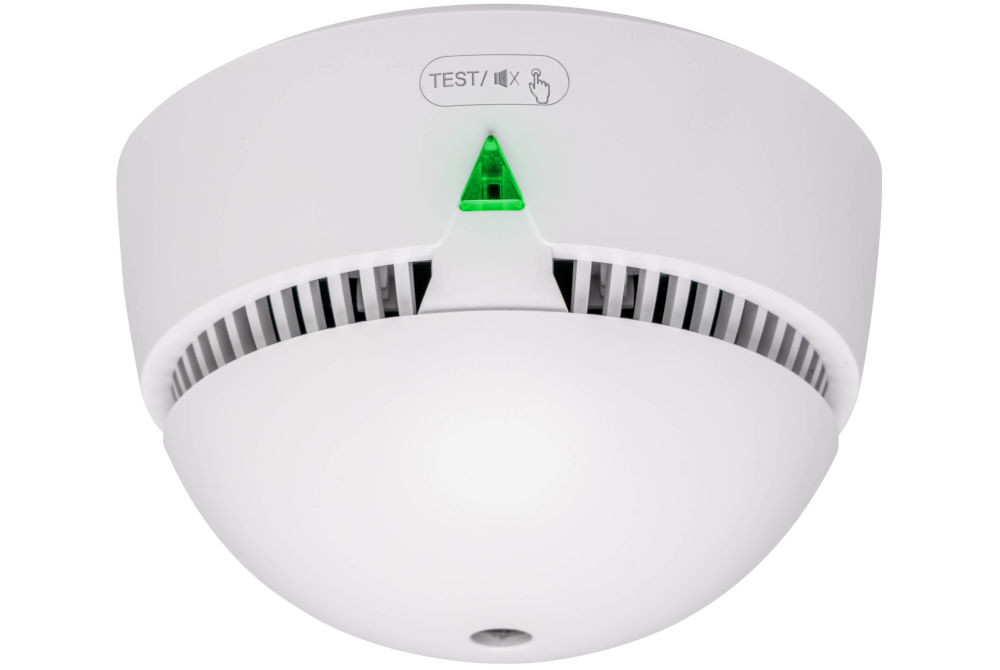 Czujnik dymu VÖGEL VSA200 Zbiorcze ujęcie z bliska miniaturowego czujnika dymu VÖGEL VSA200. Widoczne kratki wentylacyjne, zielony wskaźnik LED i oznaczenie TEST / x na przycisku.