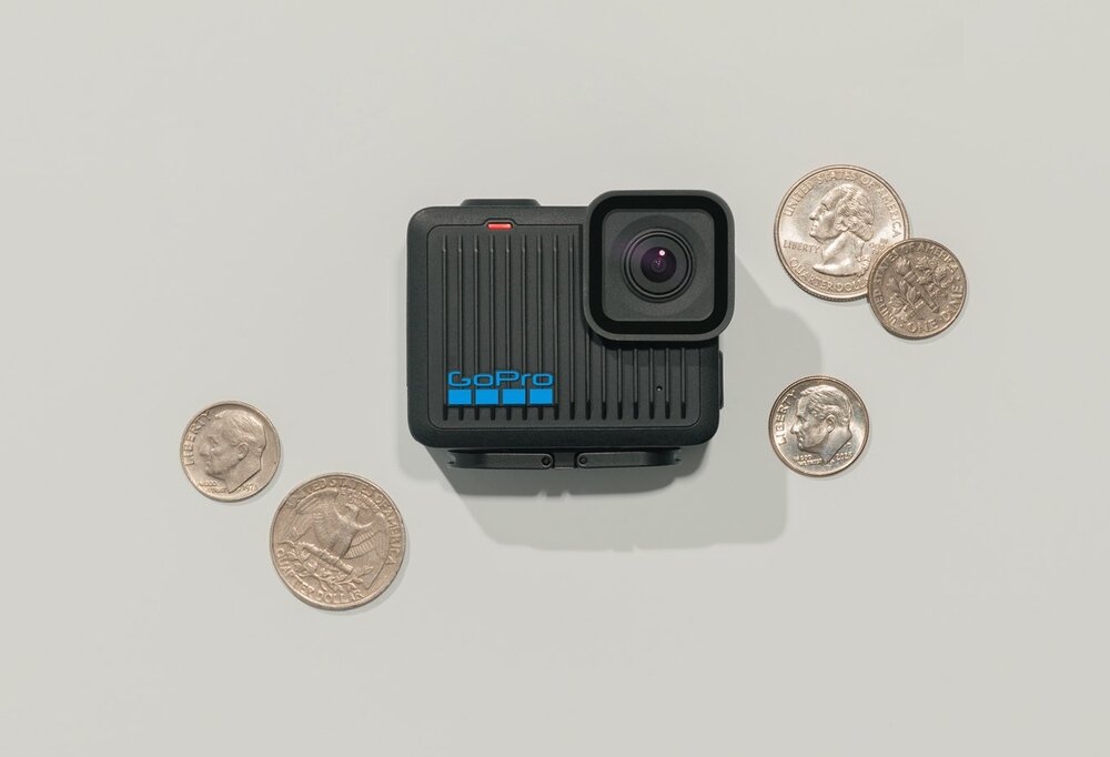 Czarna kamera sportowa z logo \'GoPro\' na obudowie, otoczona kilkoma monetami na jasnym tle.