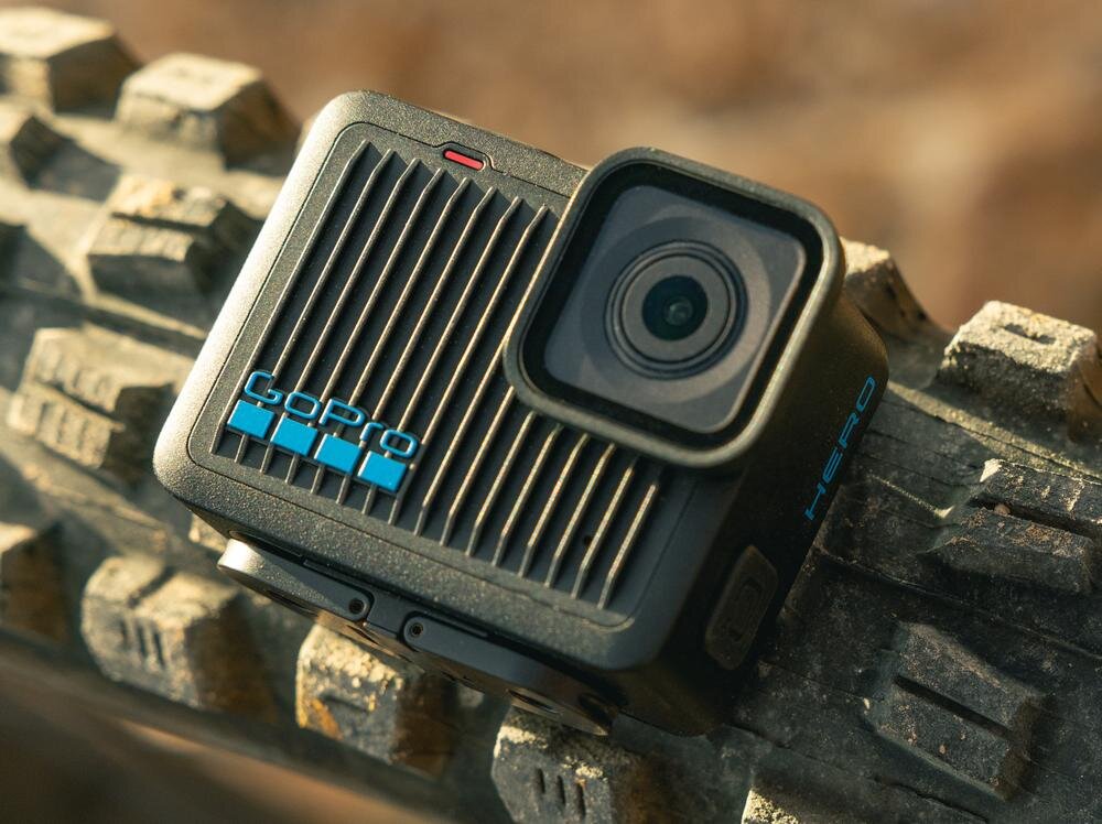 Kamera sportowa z logo \'GoPro\' i napisem \'HERO\' umieszczona na nierównej powierzchni. Obiektyw kamery jest widoczny z przodu urządzenia.