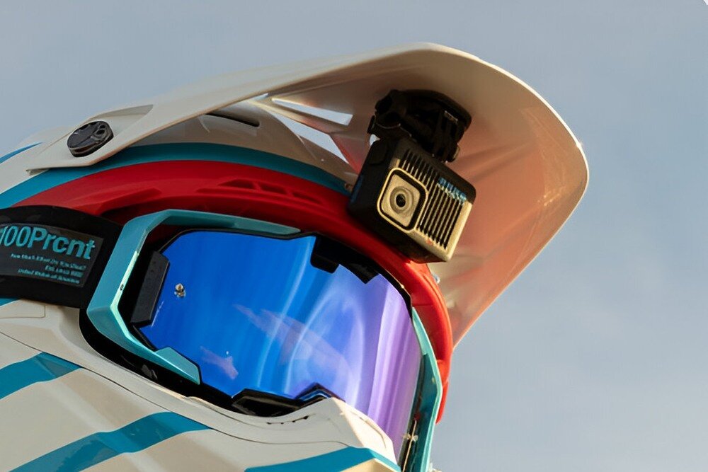 Kask z zamontowaną kamerą sportową na daszku. Na pasku gogli widoczny jest napis \'100Prcnt\'.