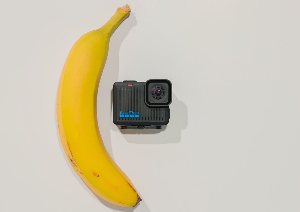 Na białym tle znajduje się żółty banan oraz czarna kamera sportowa z logo \'GoPro\' w kolorze niebieskim.