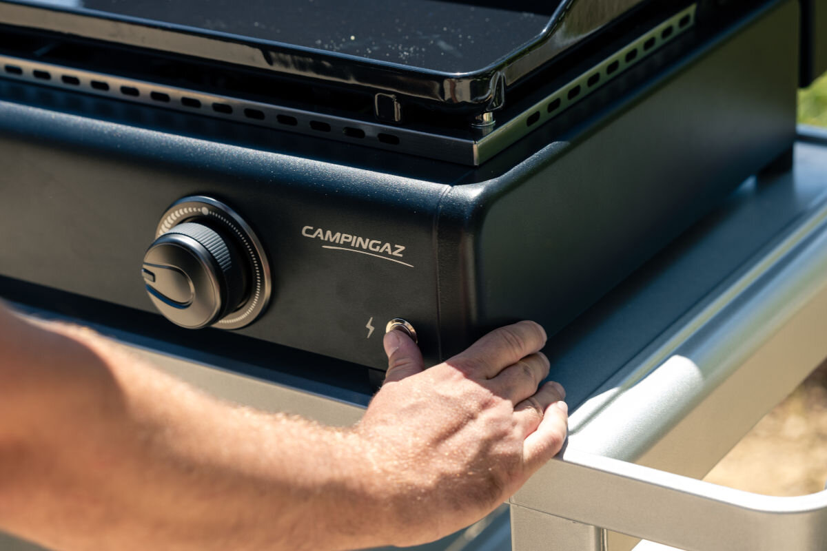 Grill gazowy CAMPINGAZ ONYX 2, rozpalanie, palniki, elektryczne, sprawnie, dłoń osoby przyciska elektroniczny palnik grilla