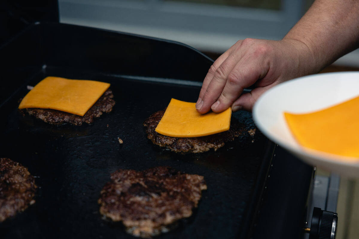 Grill gazowy CAMPINGAZ ONYX 2, szybko, dania, impreza, ogród, temperatura, osoba nakłada na mięso na grillu plastry sera