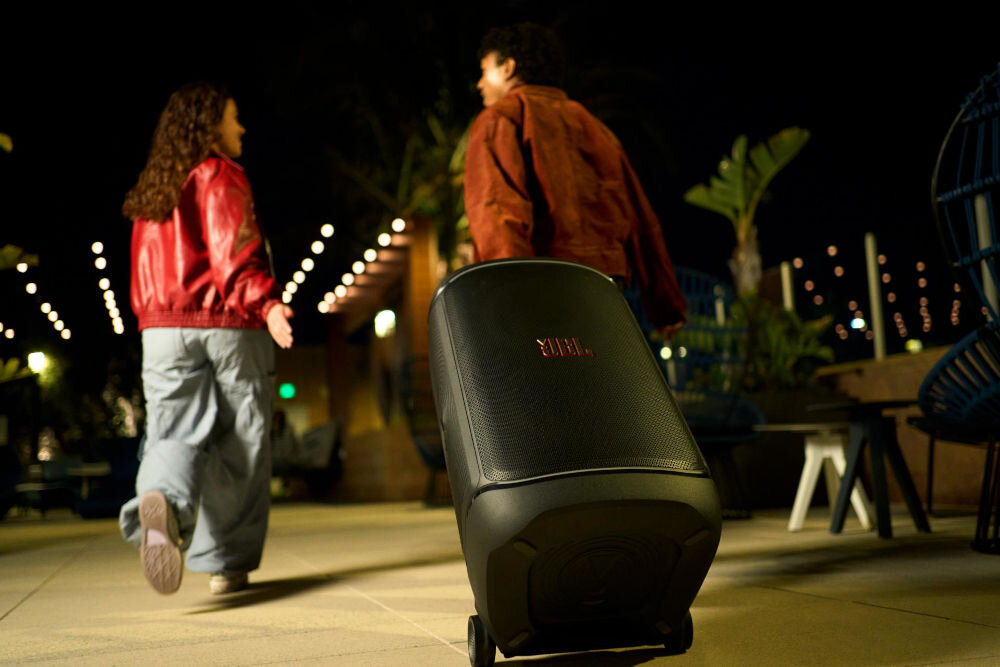 Power audio JBL PartyBox 520 - Łatwy w transporcie, Teleskopowy uchwyt, szerokie kółka, osoby idące w jednym kierunku , mężczyzna ciągnący głośnik