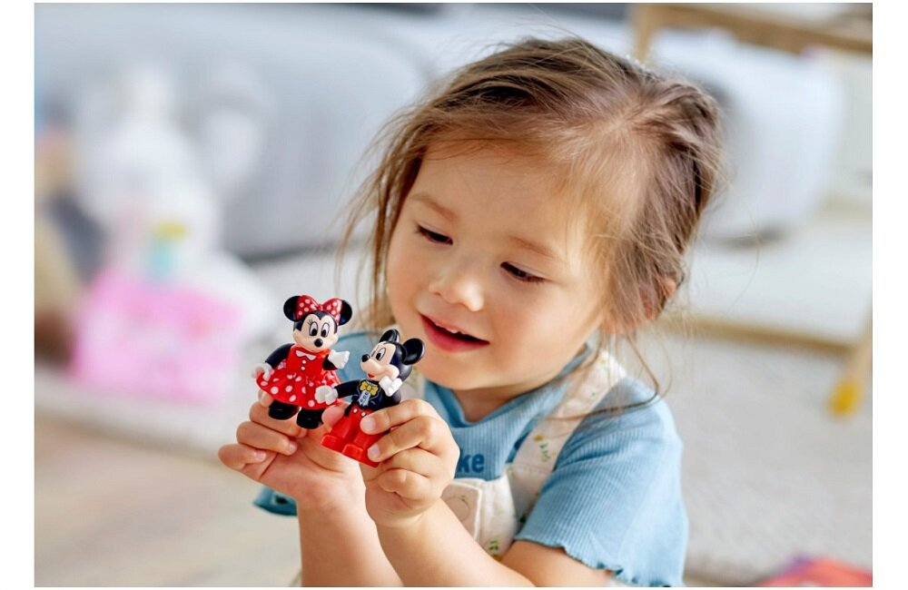 Dziecko trzyma w rękach figurki przedstawiające postacie Myszki Miki i Minnie. W tle widoczne są rozmyte elementy wnętrza pokoju.
