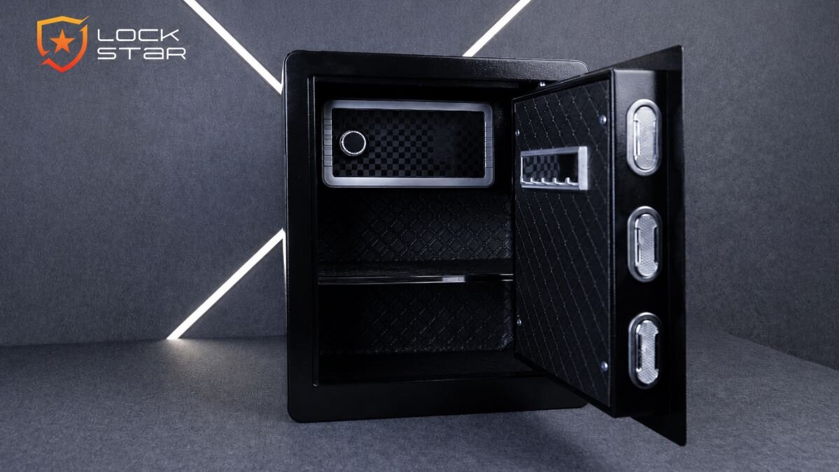 Otwarty sejf domowy z elektronicznym zamkiem, wewnątrz wyłożony materiałem o wzorze kratki. Na drzwiach widoczne są trzy srebrne pokrętła oraz logo \'LOCK STAR\'.