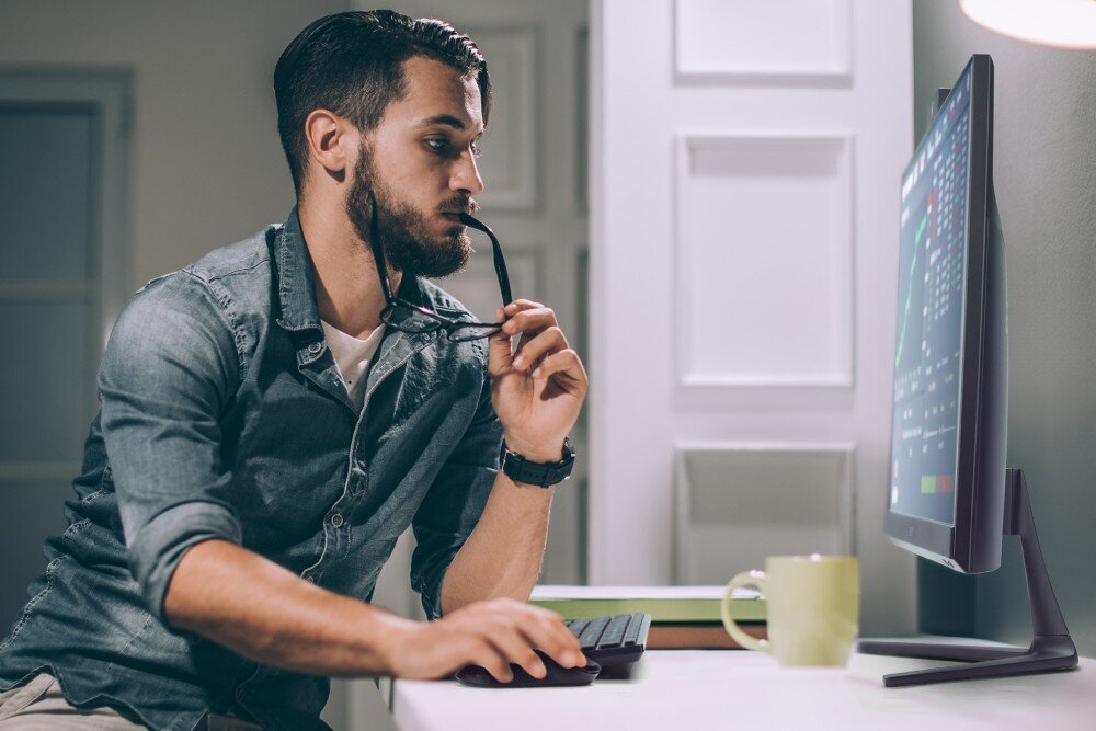 Komputer ACER Aspire C27-2E13U7UNL Mężczyzna siedzący przy biurku i pracujący na komputerze typu all-in-one, trzymający okulary w dłoni i patrzący na ekran z wykresami, typ, zastosowanie, cechy