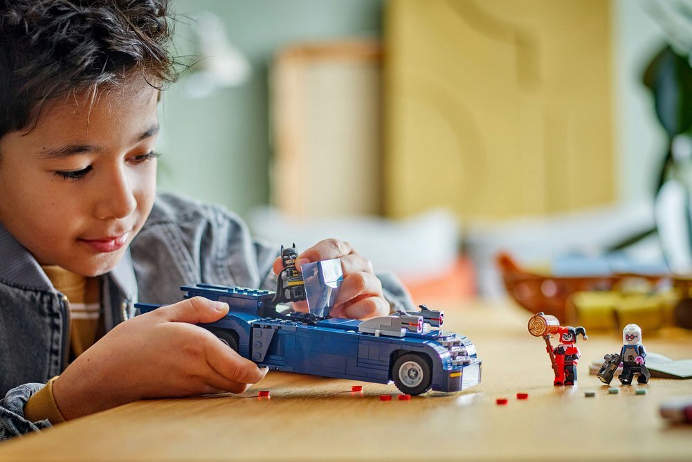 Dziecko bawi się zestawem klocków, w tym pojazdem i figurkami. Na stole znajdują się małe elementy LEGO oraz figurki postaci.