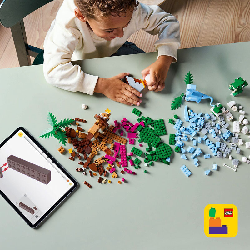 Dziecko bawi się klockami LEGO na stole, obok leży tablet z instrukcją budowy. Na dole obrazu widoczne jest logo LEGO na żółtym tle.