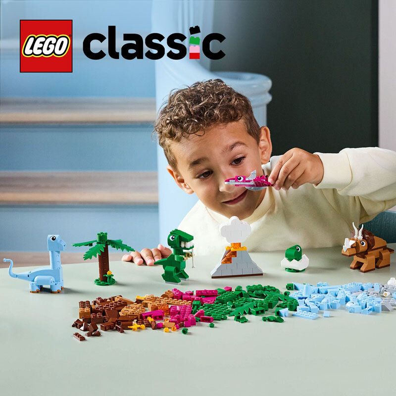 Na stole znajdują się różnokolorowe klocki LEGO oraz zbudowane z nich figurki dinozaurów i wulkanu. W tle widoczne jest logo \'LEGO classic\'.