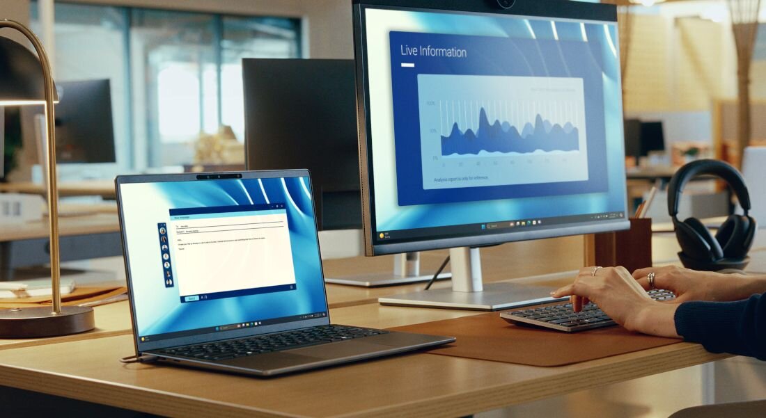 Stanowisko pracy z laptopem Dell Latitude podłączonym do monitora QHD wyświetlającego wykresy Live Information obok słuchawek i klawiatury w biurze. - Ekran QHD+ 16:10 