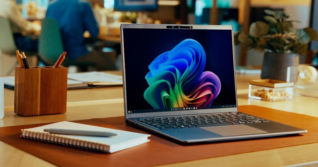 Laptop Dell Latitude z Windows 11 ARM wyświetlający kolorową abstrakcyjną tapetę na drewnianym biurku z organizerem na długopisy, notatnikiem i rozmytym tłem biurowym.  - Windows 11 ARM na Snapdragon  
