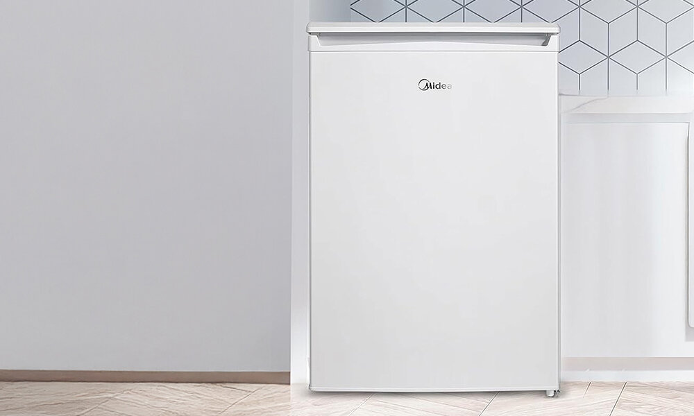 LODÓWKA MIDEA MDRD168FGE01 Lodówka w kolorze białym z zamkniętymi drzwiami ustawiona w jasnej, minimalistycznej kuchni kompaktowy rozmiar małe mieszkanie funkcjonalność oszczędność miejsca