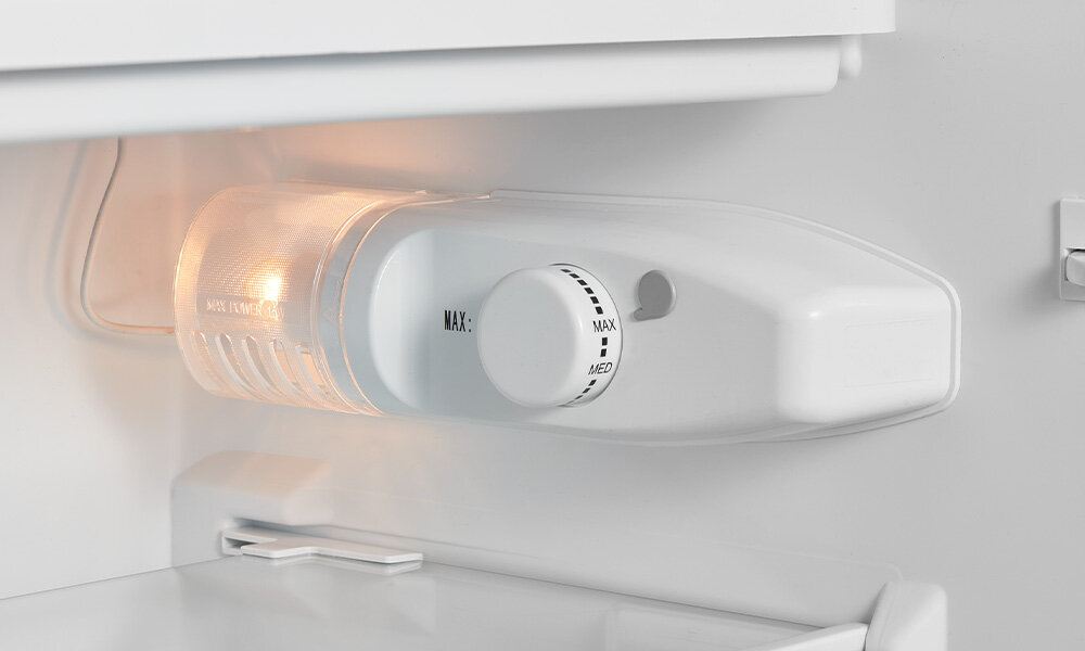 LODÓWKA MIDEA MDRD142FGE50 Zdjęcie przedstawia oświetlony regulator temperatury wewnątrz lodówki, z widoczną pokrętłem ustawiania poziomu chłodzenia. Obok znajduje się delikatnie świecąca lampka, podkreślająca jasne, czyste wnętrze urządzenia regulacja temperatury pokrętło chłodzenie ustawienia min max med