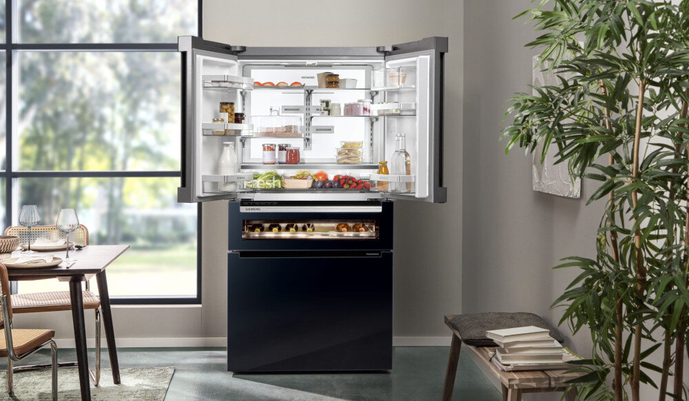 LODÓWKA SIEMENS KF96RSBEA Otwarta lodówka Siemens ustawiona przy dużym oknie pokazuje uporządkowane półki z żywnością. Widoczne jest połączenie części chłodzącej i zamrażarki w jednej bryle lodówka French Door 572 l No Frost czarny szklany front dużo miejsca na produkty pojemna dla dużej rodziny