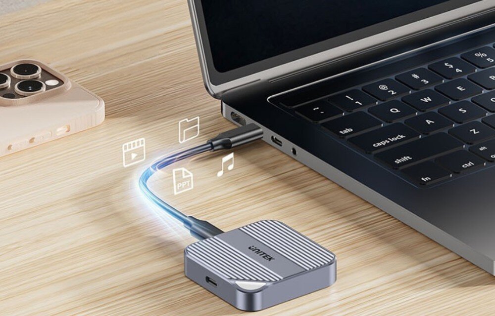 Obudowa dysku UNITEK S1244AGY01 Przenośne urządzenie Unitek podłączone kablem USB-C do bocznego portu otwartego laptopa na drewnianym blacie. Nad kablem widoczne są białe ikony symbolizujące transfer plików wideo, muzycznych oraz dokumentów tekstowych