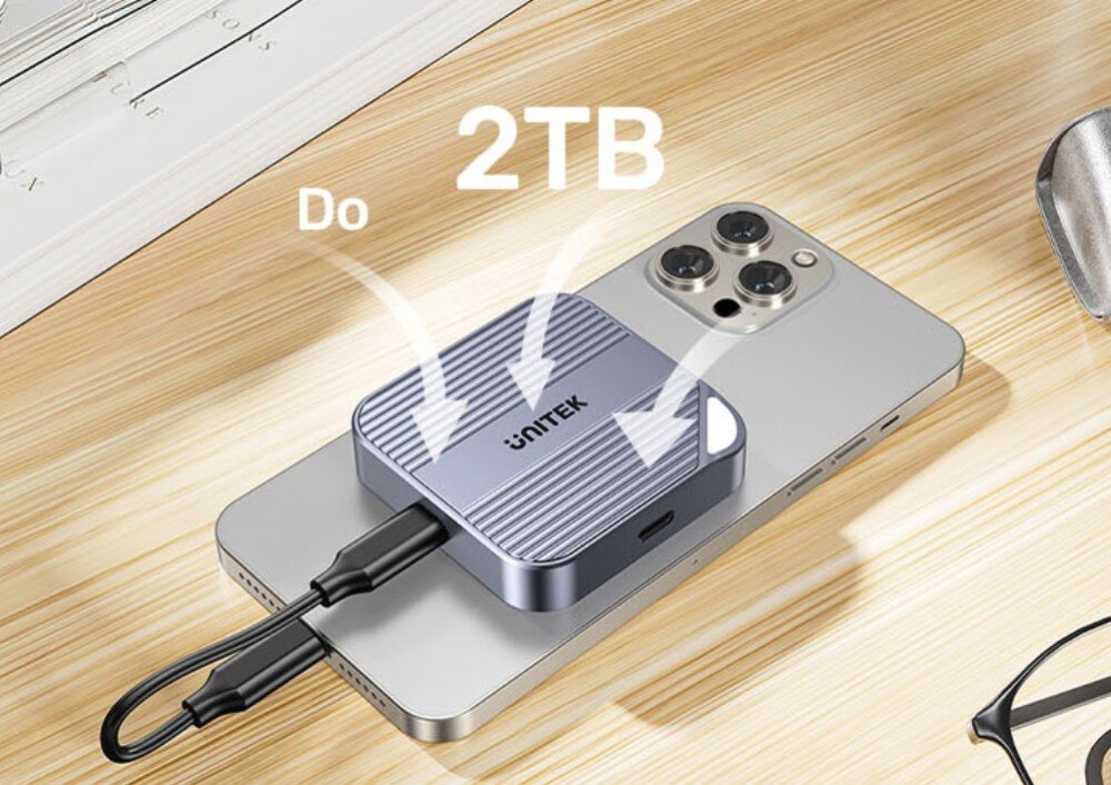 Obudowa dysku UNITEK S1244AGY01 Szare akcesorium Unitek o żebrowanej powierzchni przytwierdzone do pleców smartfona. Nad urządzeniem widnieje biały napis 2TB ze strzałkami wskazującymi na obudowę, co sugeruje dużą pojemność pamięci