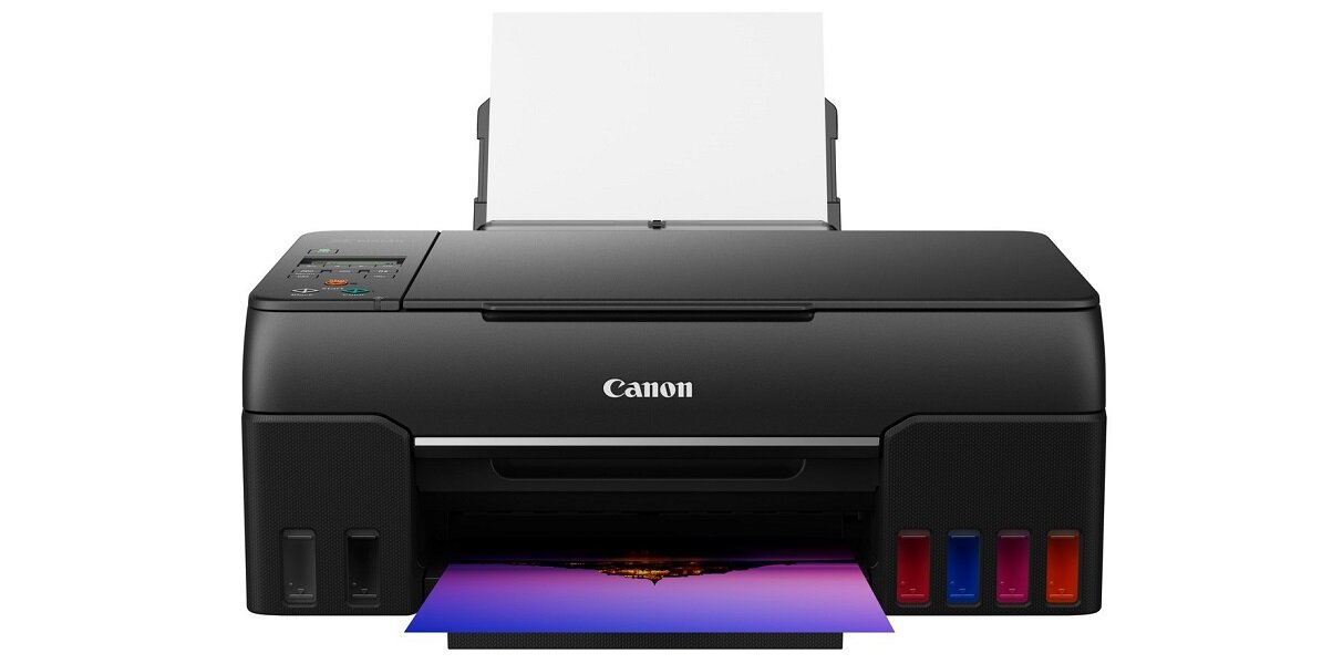 Czarne urządzenie wielofunkcyjne z logo Canon, z widocznymi pojemnikami na tusz i wydrukowanym kolorowym zdjęciem. Na górze znajduje się podajnik papieru z kilkoma arkuszami.