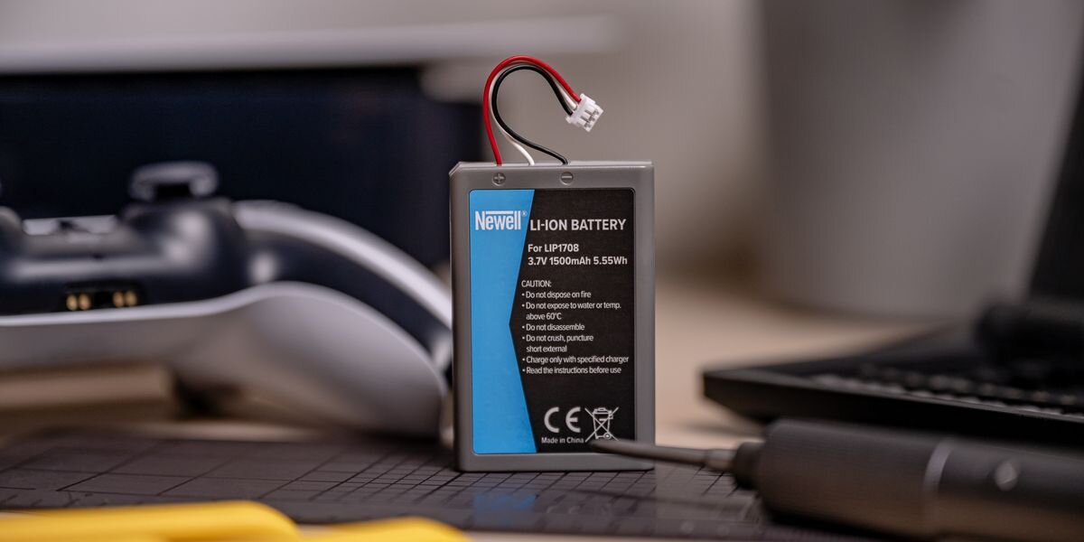 Akumulator NEWELL 1500 mAh LIP1708 do kontrolera DualSense Sony PlayStation 5, Pionowe ujęcie baterii Newell 1500 mAh na macie serwisowej, w tle widoczny rozmazany biały kontroler do gier, bezłutowniczo, złącze, ergonomia