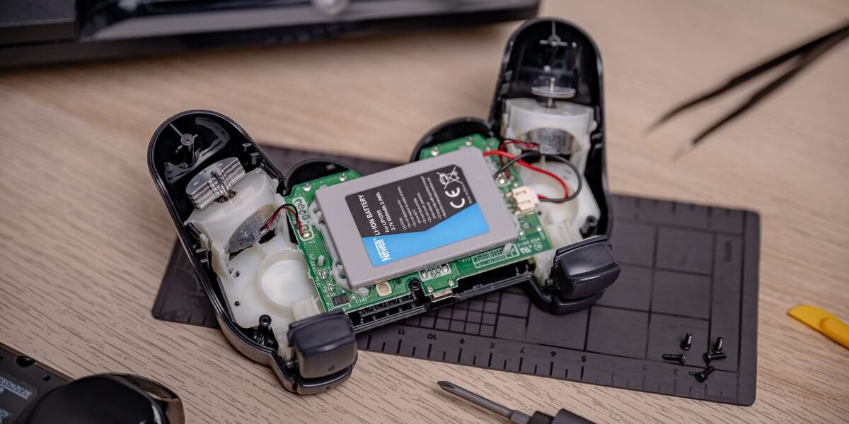 Akumulator NEWELL 650 mAh LIP1359 do kontrolera DualShock 3 Sony PlayStation 3, Wnętrze rozkręconego czarnego kontrolera do gier z widocznym szarym akumulatorem Newell i silniczkami wibracji, pad, zasilanie, moc, ładowanie