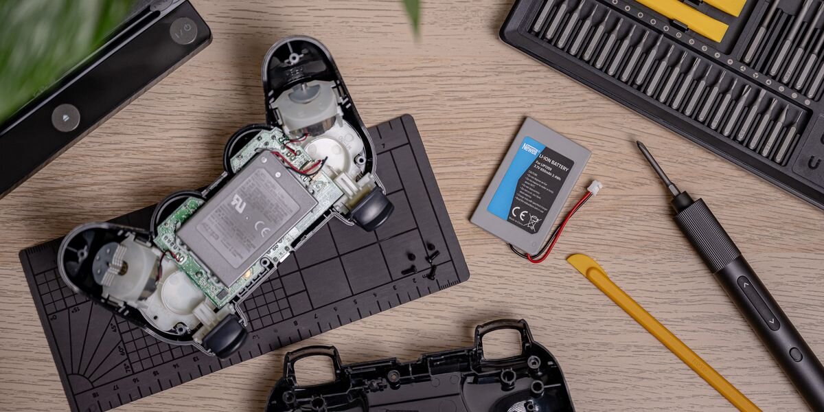 Akumulator NEWELL 650 mAh LIP1359 do kontrolera DualShock 3 Sony PlayStation 3, Rozkręcony kontroler, nowy akumulator Newell, śrubokręt i zestaw bitów na drewnianym blacie. Widok z góry, 650mAh, Li-ion, 3,7V, DualShock3