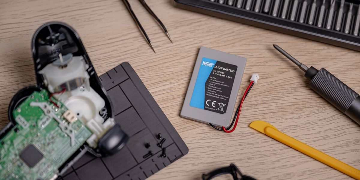Akumulator NEWELL 650 mAh LIP1359 do kontrolera DualShock 3 Sony PlayStation 3, Szary akumulator Newell obok rozkręconego kontrolera, pęsety i śrubokręta na ciemnej macie serwisowej, dokładne, bezadapterowy, lekki, ergonomiczny