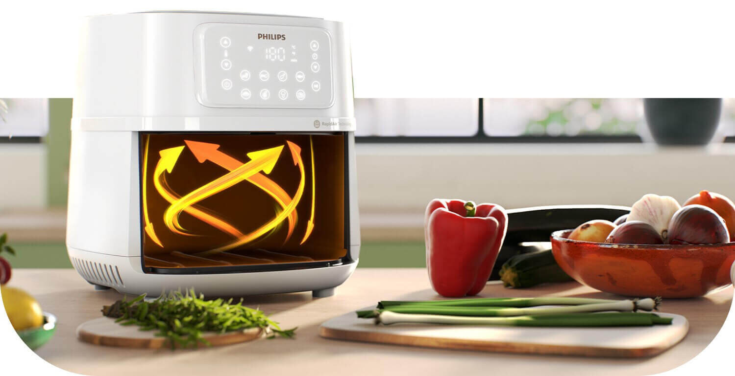 Na blacie kuchennym stoi biała frytkownica beztłuszczowa z wyświetlaczem dotykowym, na którym widnieje logo PHILIPS. Obok urządzenia znajdują się świeże warzywa, takie jak papryka, cebula i pomidory w misce.