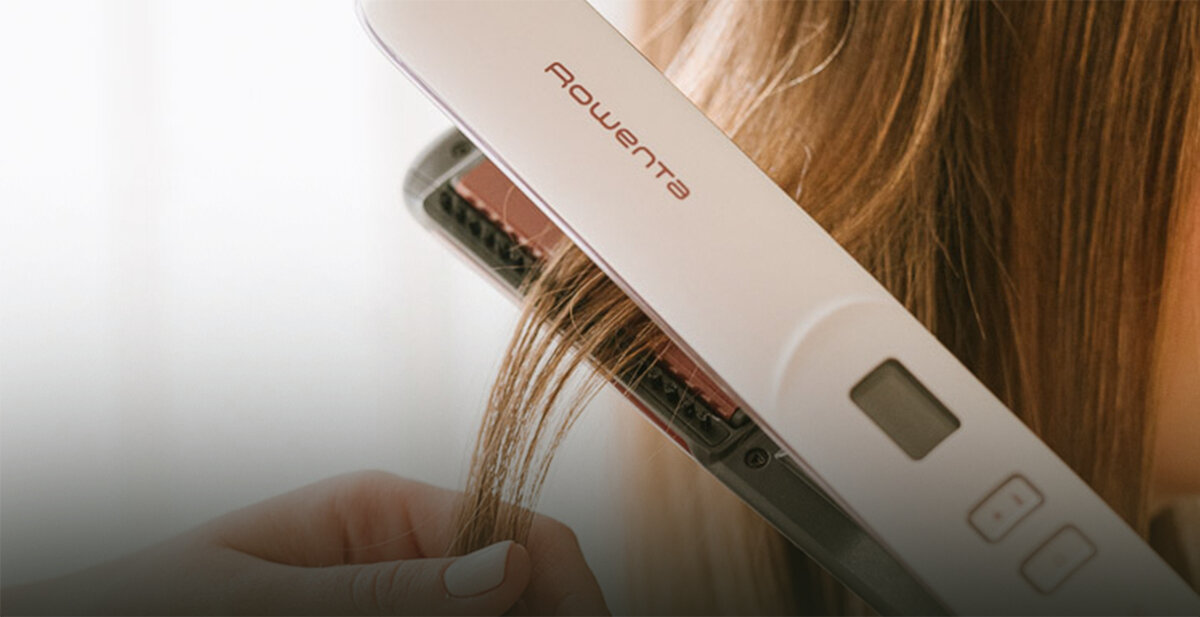 Prostownica do włosów z widocznym logo \'ROWENTA\' jest używana do prostowania pasma włosów. Urządzenie ma wyświetlacz i dwa przyciski sterujące.