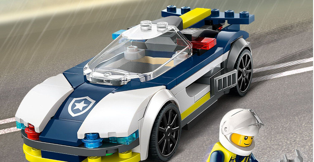 Na obrazie widoczny jest zestaw klocków LEGO przedstawiający sportowy samochód policyjny z przezroczystą kabiną i kolorowymi światłami. Obok samochodu stoi figurka LEGO w kasku.