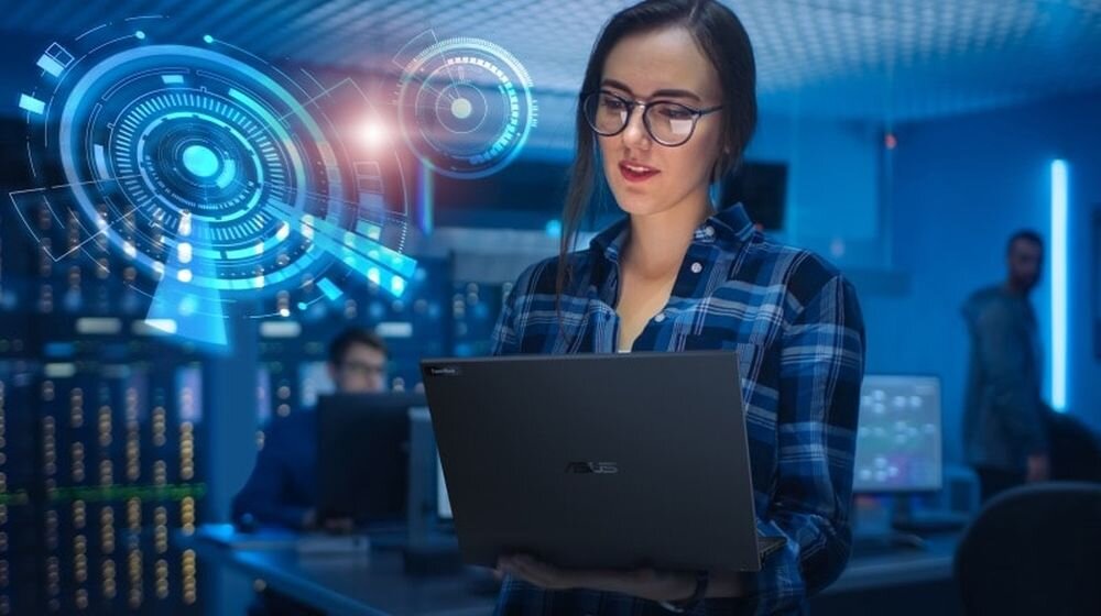 Profesjonalistka w okularach i kraciastej koszuli pracująca na laptopie ASUS ExpertBook B5 w nowoczesnym biurze z technologią AI, futurystyczne holograficzne interfejsy w kolorze niebieskim, zaawansowane funkcje sztucznej inteligencji do pracy biznesowej, dobre rozwiązanie dla specjalistów IT i managerów  - AI 
