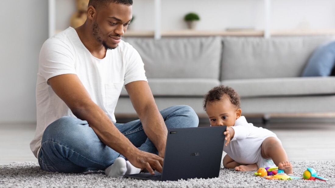 Ojciec pracujący na laptopie ASUS ExpertBook B5 w domu, siedząc na dywanie obok bawiącego się dziecka, symbolizujący elastyczność pracy zdalnej i ekologiczne podejście dzięki certyfikatowi EPEAT Gold. - EPEAT Gold