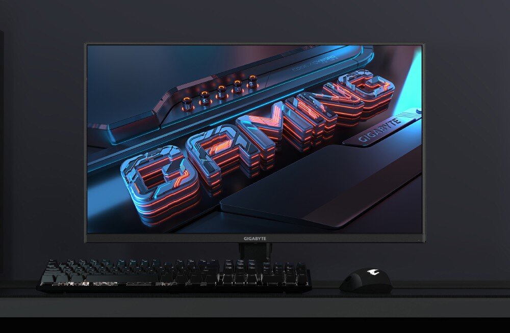 Monitor GIGABYTE G25F2 Ekran komputera na biurku z wyświetlonym trójwymiarowym napisem 'GAMING' w kolorach niebieskim i czerwonym, widoczna klawiatura i myszka przed monitorem, opis