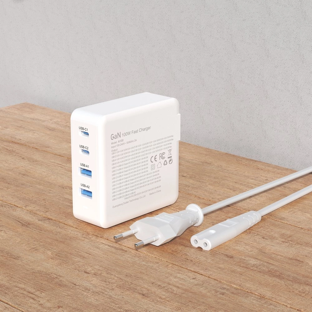 Biała szybka ładowarka sieciowa GaN 100W z dwoma portami USB-C i dwoma portami USB-A, leży na drewnianej powierzchni. Obok znajduje się biały kabel z wtyczką elektryczną.