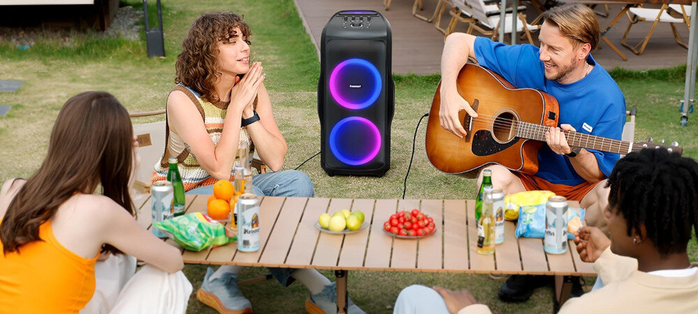 Power Audio TRONSMART Halo 300 27000 mAh do 20 godzin odtwarzania długa praca, osoby siedzące przy stoliku na świeżym powietrzu, power audio stojące na trawie z podłączoną gitarą