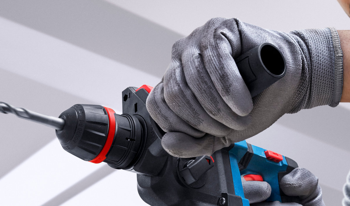 BOSCH Professional GBH 18V-18 X 0611927102 1,8 kg bez akumulatora ergonomiczny uchwyt cięższymi młotami antypoślizgowa powierzchnia rękojeści - Zbliżenie na dłonie w rękawicach ochronnych trzymające młot udarowo-obrotowy podczas pracy.