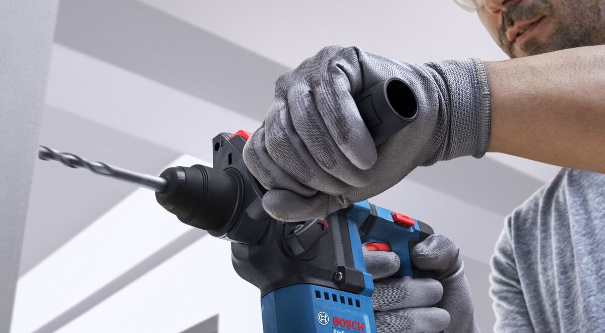 BOSCH Professional GBH 18V-18 0611927001 1,6 kg bez akumulatora ergonomiczny uchwyt cięższymi młotami antypoślizgowa powierzchnia rękojeści - Zbliżenie na dłonie w rękawicach ochronnych trzymające młot udarowo-obrotowy podczas pracy.