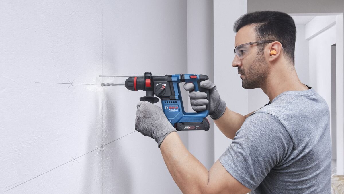 BOSCH Professional GBH 18V-18 X 0611927101 BOSCH Professional GBH 18V-18 X 0611927101 beton, cegła czy kamień wykonywać otwory dłutować fragmenty powierzchni - Mężczyzna w okularach ochronnych wierci otwór w ścianie za pomocą akumulatorowego młota udarowo-obrotowego