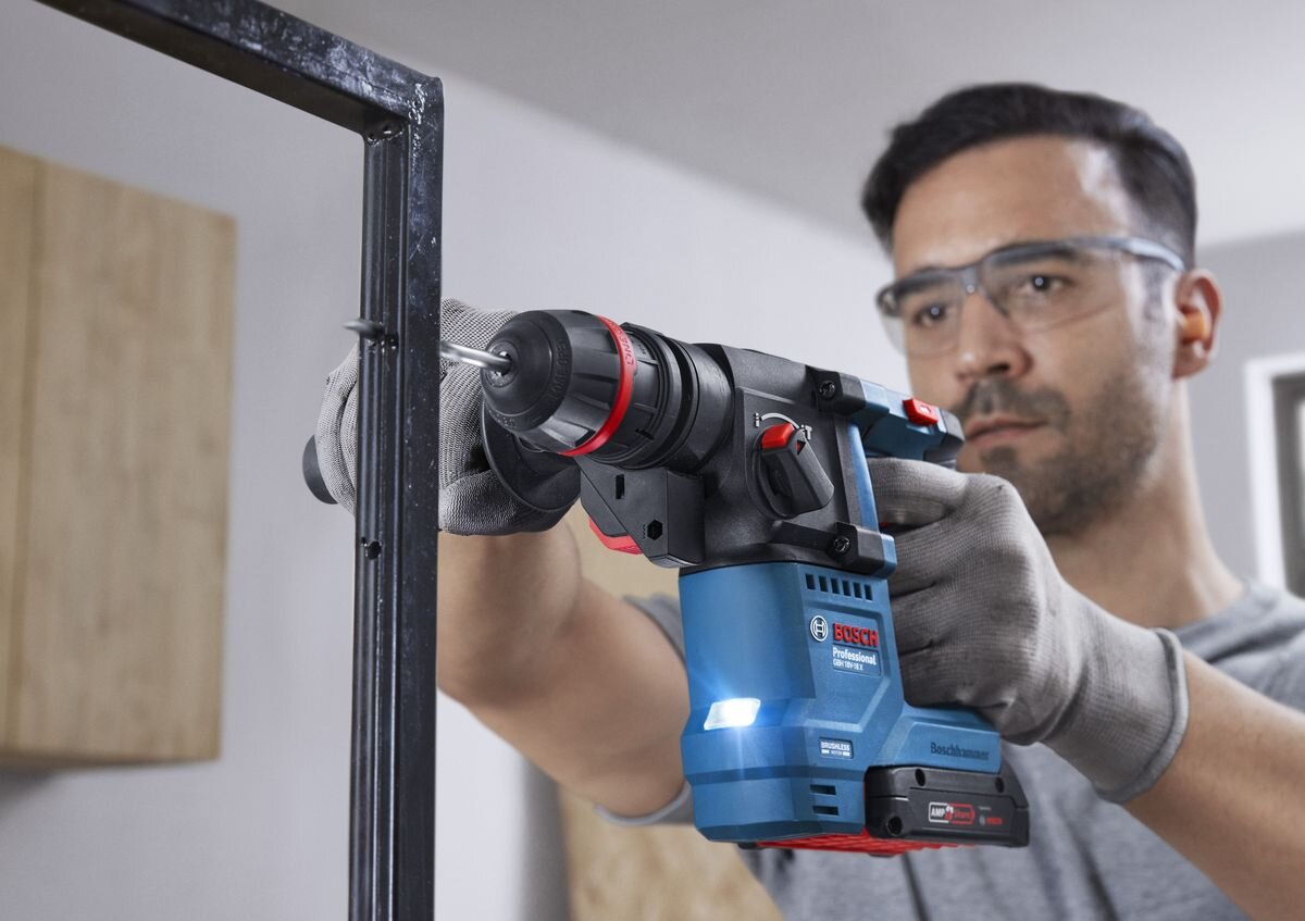 BOSCH Professional GBH 18V-18 X 0611927101 obsługuje wiertła SDS plus 4–18 mm 4–10 mm wiertarkami uniwersalnymi twardymi materiałami uchwyt ONECHUCK chwycie cylindrycznym sześciokątnym 10 mm - Mężczyzna wierci otwór w metalowym elemencie, używając młota udarowo-obrotowego